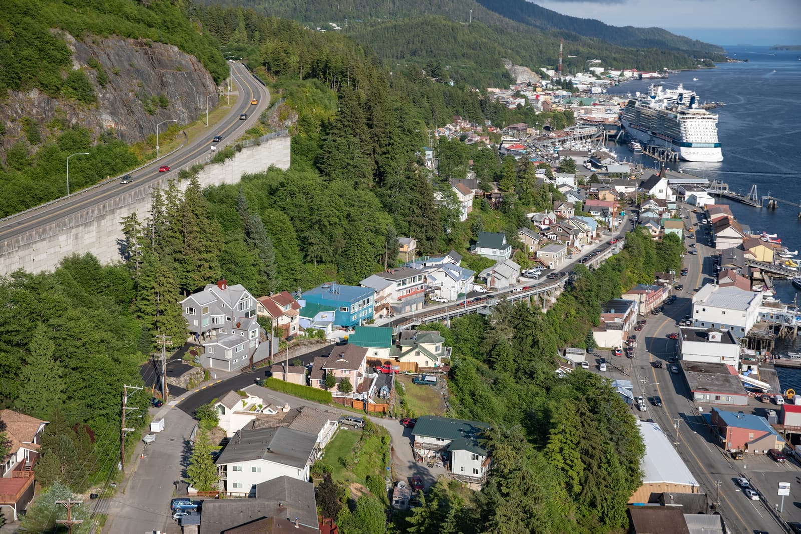 Aerial view of Ketchikan squeezed between forested hills and the Tongass Narrows, with a cruise ship at the dock